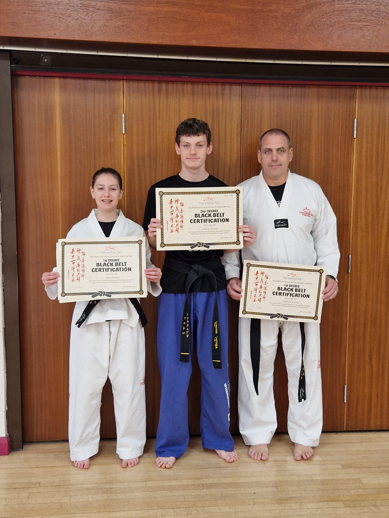 Lucas Foster holding his 2nd Degree Black Belt certification alongside Mr Cook and another student