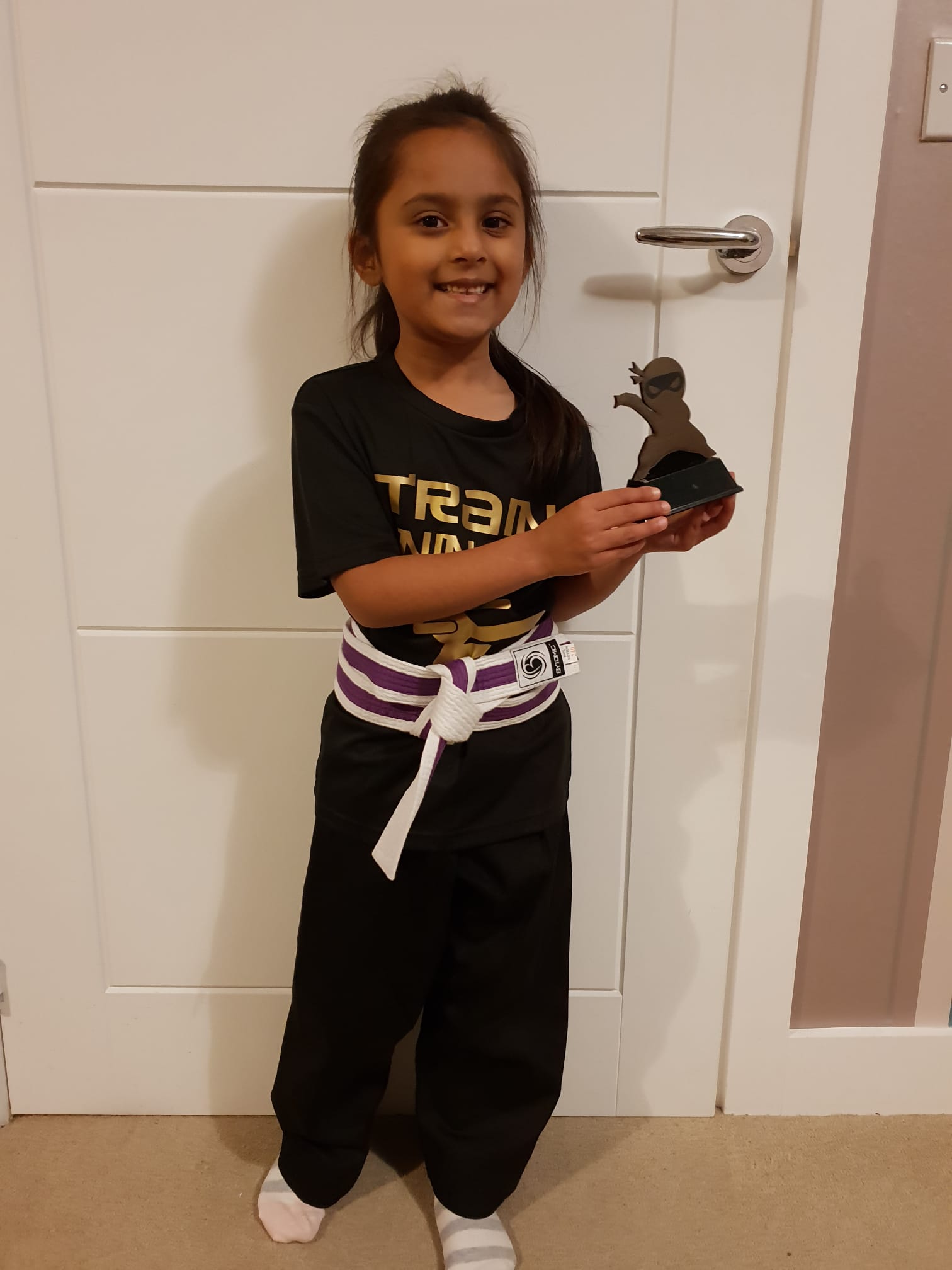 Prisha holding her Ninja Skillz trophy in her Train Taekwondo t-shirt with purple stripe belt