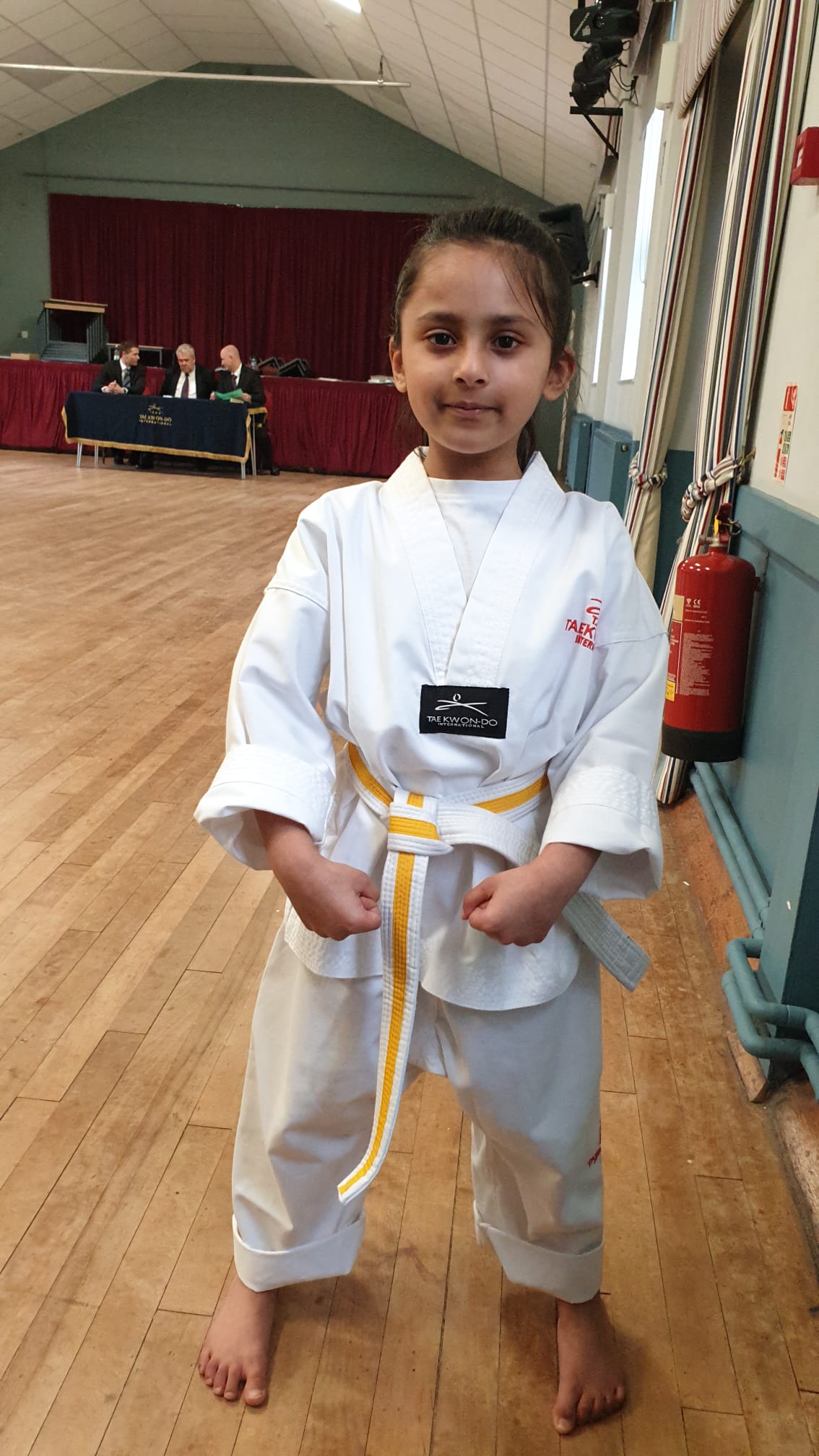 Prisha at a TAGB grading in her white dobok with yellow belt